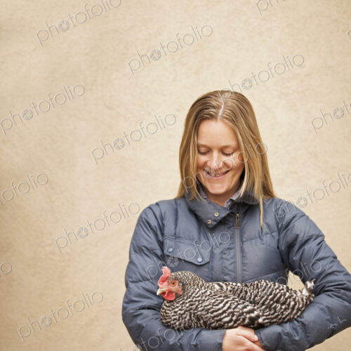 A woman wearing a grey coat and holding a chicken. A woman wearing a grey coat and holding a chicken.