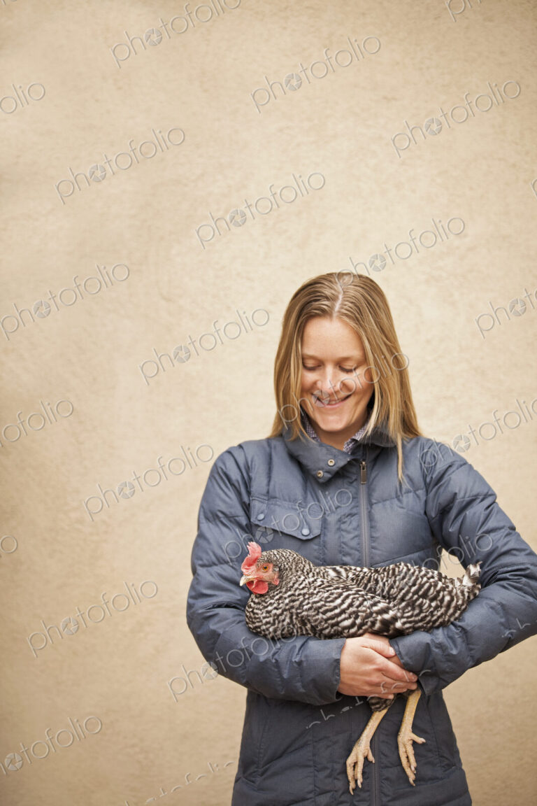 A woman wearing a grey coat and holding a chicken.