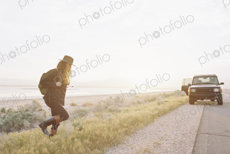 A woman wearing a hat and carrying a backpack near a 4x4 car,