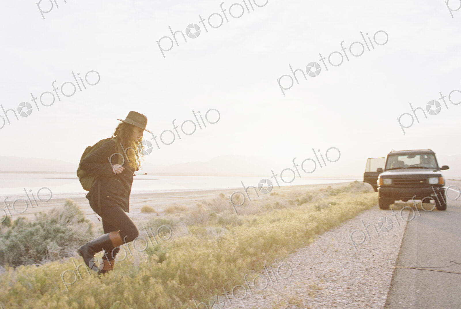 A woman wearing a hat and carrying a backpack near a 4×4 car,