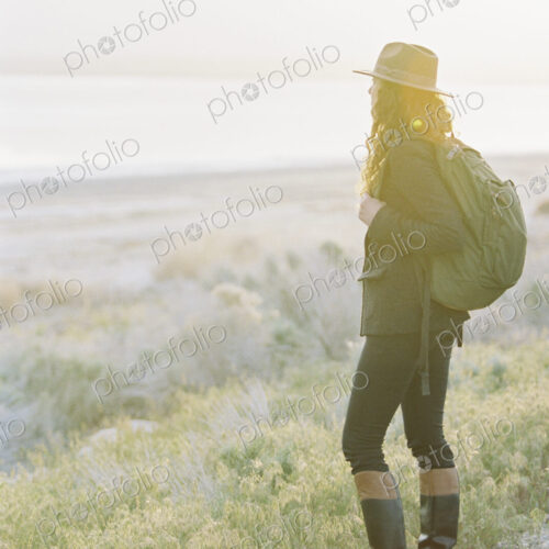 A woman wearing a hat and carrying a backpack, standing on a path overlooking a lake… A woman wearing a hat and carrying a backpack, standing on a path overlooking a lake…