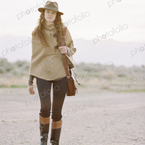 A woman wearing a hat and carrying a leather bag.