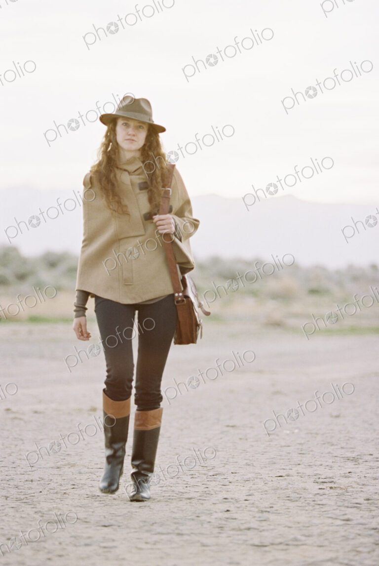 A woman wearing a hat and carrying a leather bag.