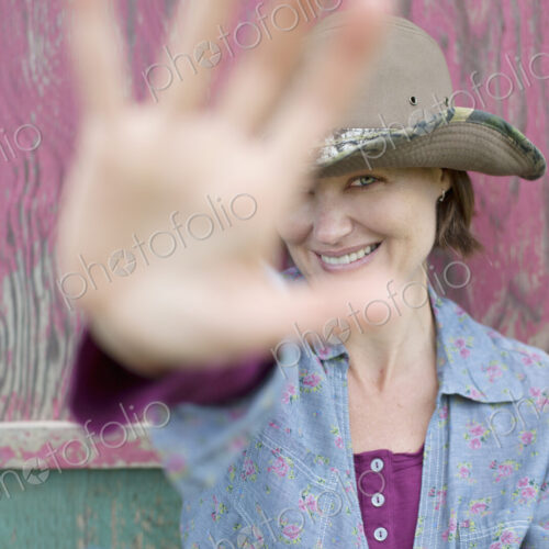 A woman wearing a hat with a wide brim, holding her hand out to block the view of her… A woman wearing a hat with a wide brim, holding her hand out to block the view of her…