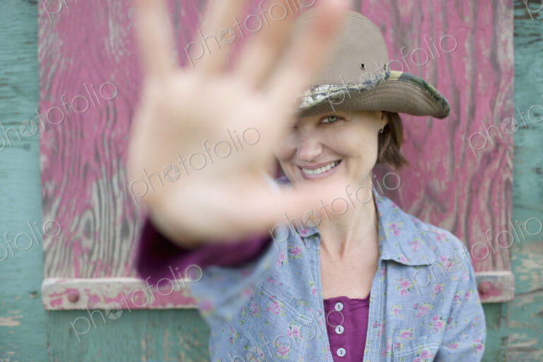 A woman wearing a hat with a wide brim, holding her hand out to block the view of her…