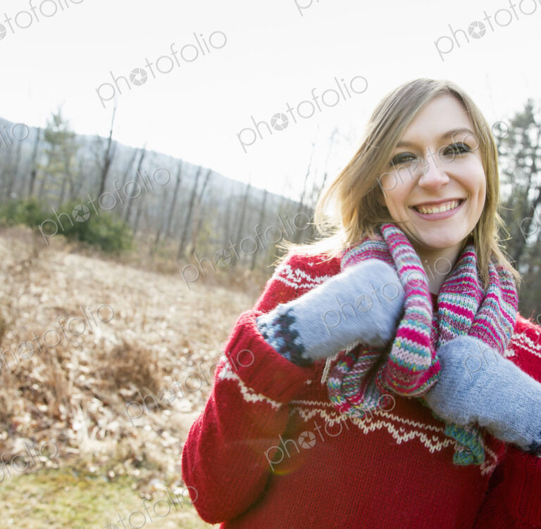 A woman wearing a knitted scarf and woolen mittens outdoors on a winter day.