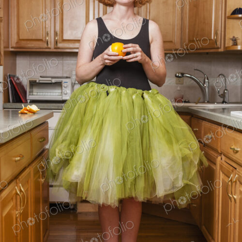 A woman wearing a lime green ballet tutu, standing in a ballet position in her kitchen.