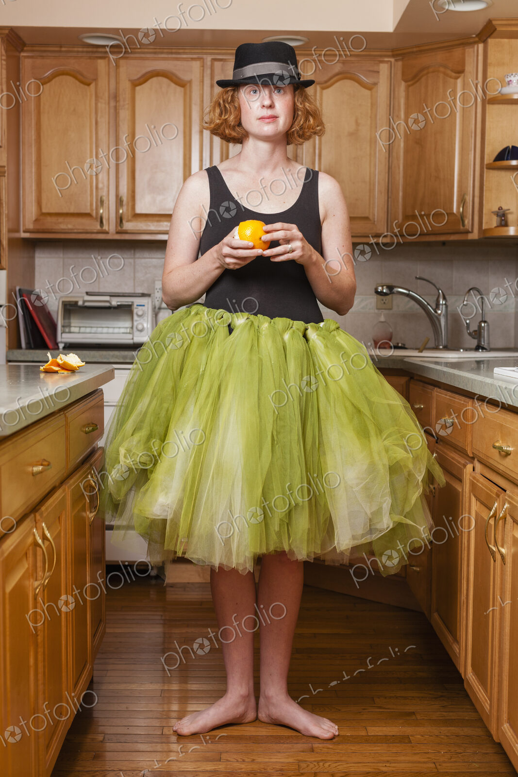 A woman wearing a lime green ballet tutu, standing in a ballet position in her kitchen.