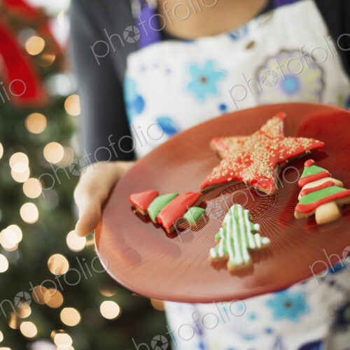 A woman wearing an apron holding a plate of organic decorated Christmas cookies. A woman wearing an apron holding a plate of organic decorated Christmas cookies.