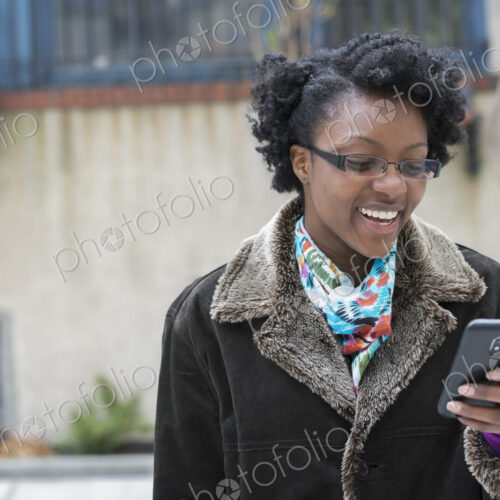 A woman wearing glasses, looking at her smart phone, keeping in touch while on the go.