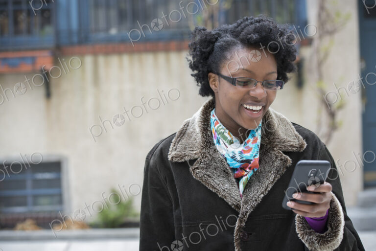A woman wearing glasses, looking at her smart phone, keeping in touch while on the go.
