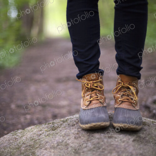 A woman wearing walking boots and jeans, standing on a stone beside a path in woodland. A woman wearing walking boots and jeans, standing on a stone beside a path in woodland.