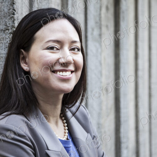 A woman with a grey jacket standing by a wall. A woman with a grey jacket standing by a wall.