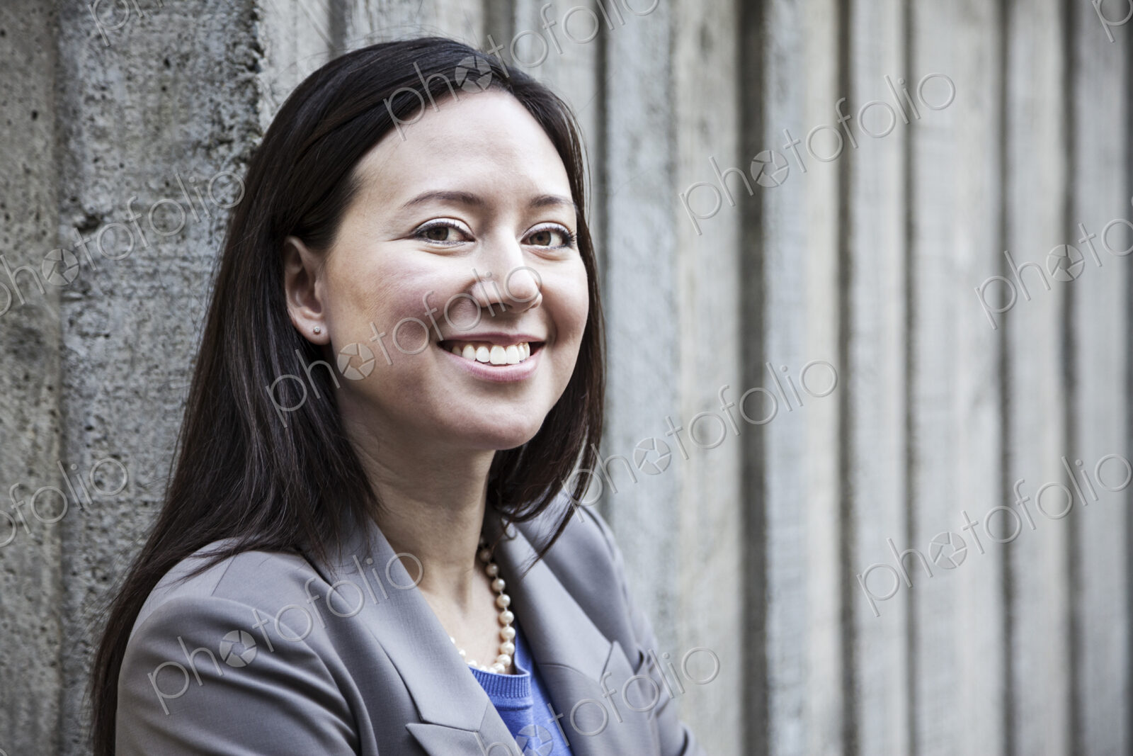 A woman with a grey jacket standing by a wall.