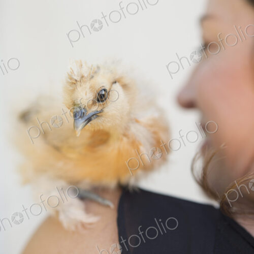 A woman with a small fluffy chick bird perched on her shoulder.