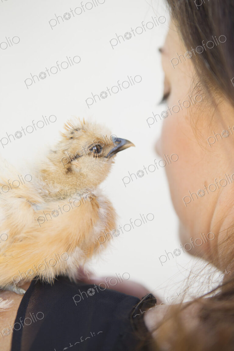 A woman with a small fluffy chick bird perched on her shoulder.