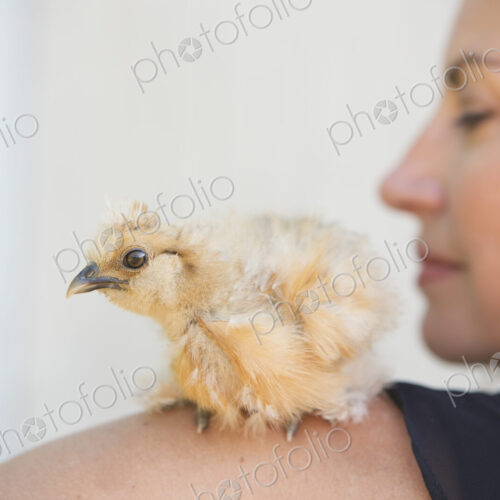 A woman with a small fluffy chick bird perched on her shoulder.