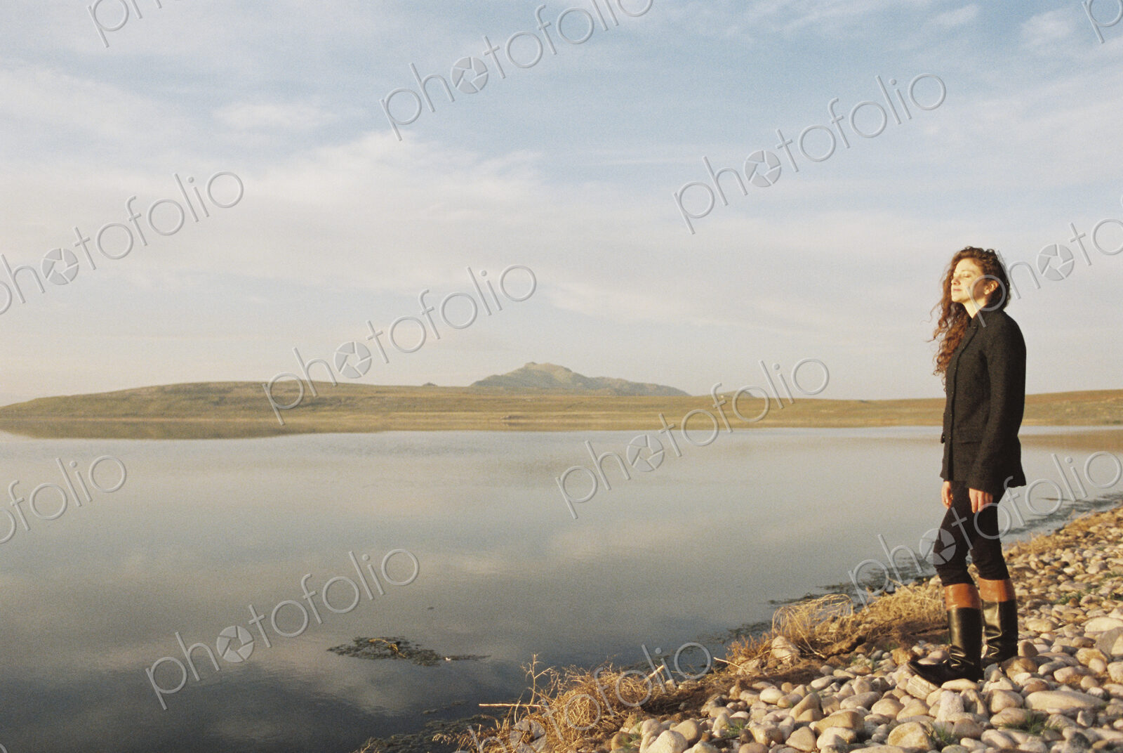 A woman with curly hair standing on the shore of a lake.