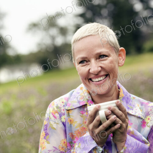 A woman with her hands wrapped around a coffee cup, sitting on a meadow. A woman with her hands wrapped around a coffee cup, sitting on a meadow.