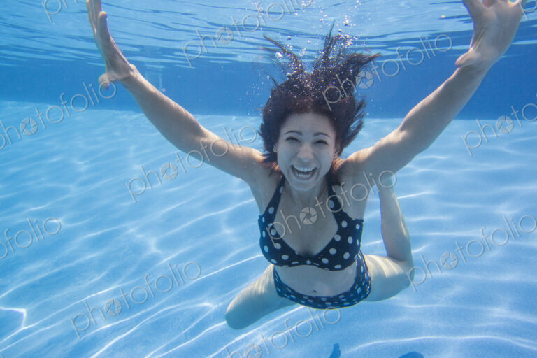 A woman with long black hair wearing a spotted bikini, underwater.