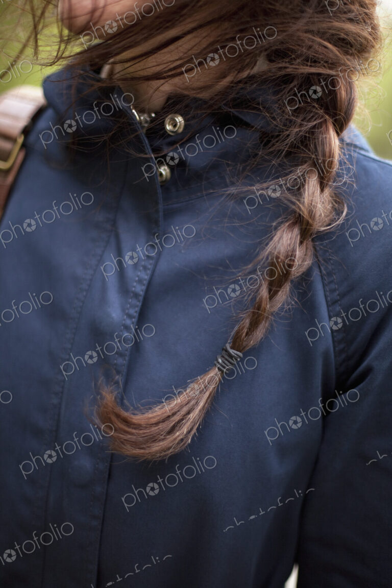 A woman with long brown hair plaited in a braid. Wearing a blue leather jacket. Close up.