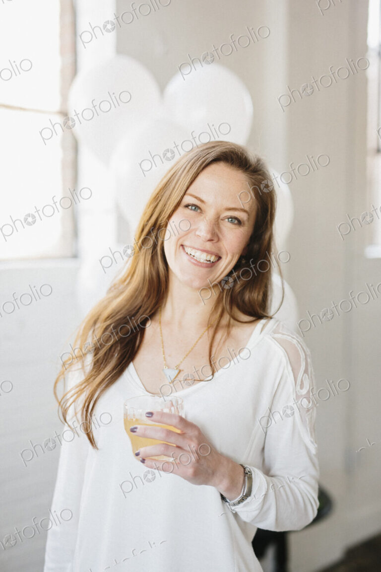 A woman with long hair in a white blouse, holding a drink. White balloons, party…