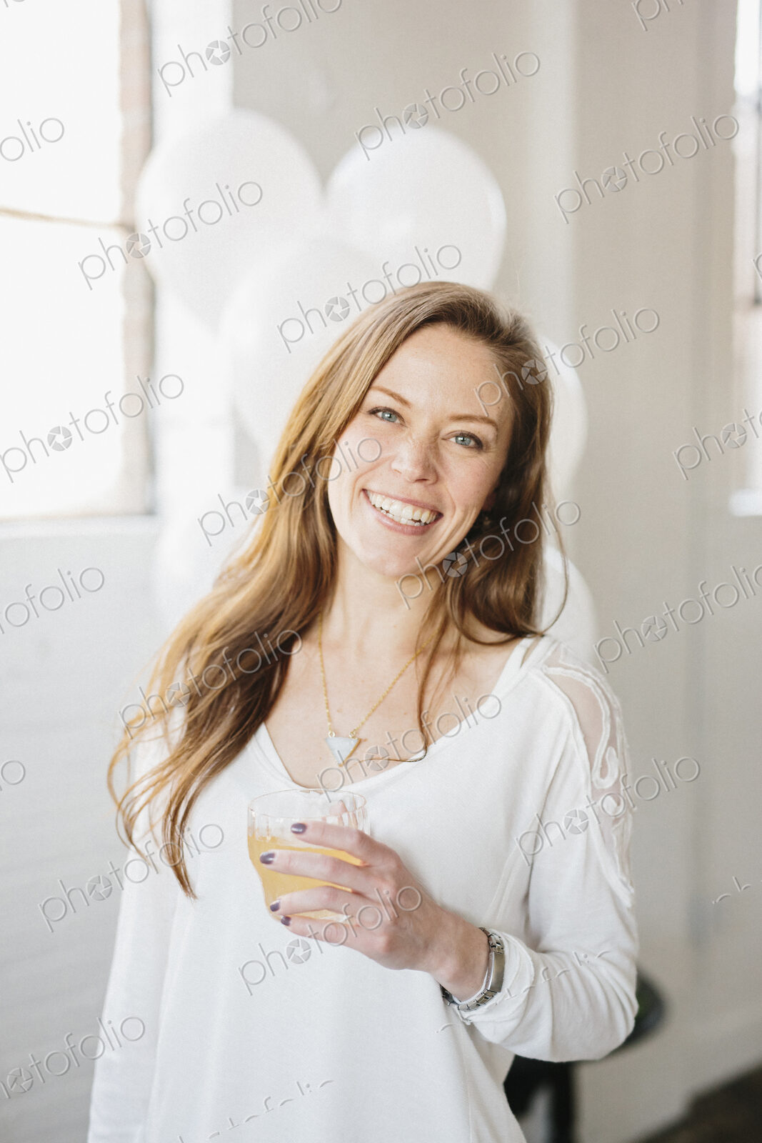 A woman with long hair in a white blouse, holding a drink. White balloons, party…