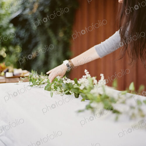 A woman with long hair leaning over a table laid outside with a white cloth and a… A woman with long hair leaning over a table laid outside with a white cloth and a…