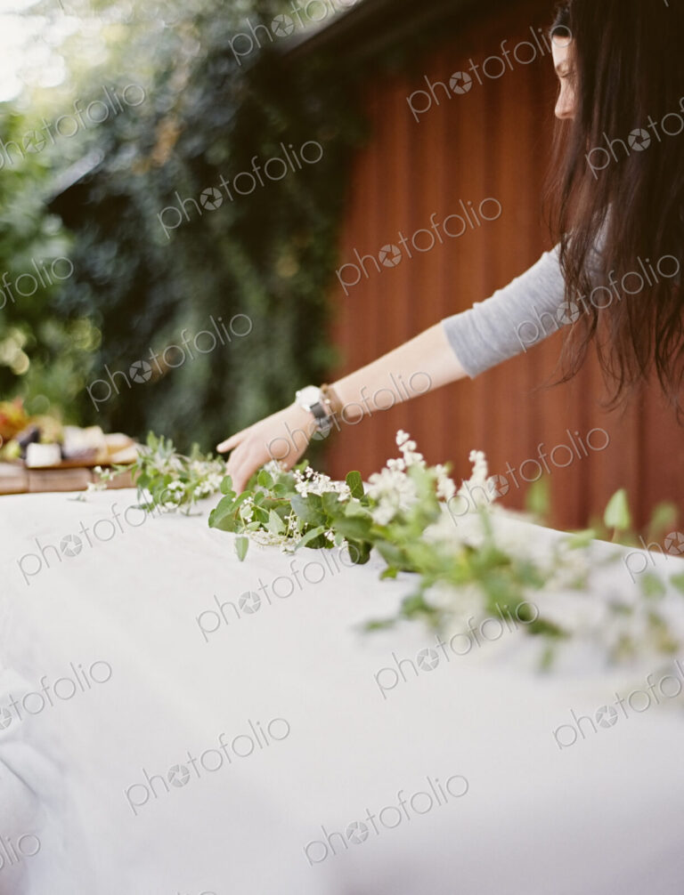 A woman with long hair leaning over a table laid outside with a white cloth and a…