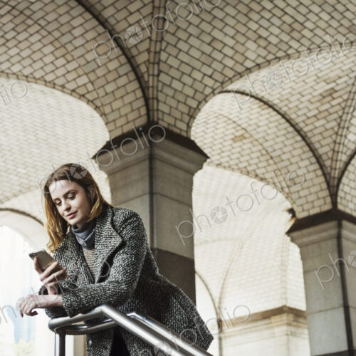 A woman with long hair looking at her smart phone, under an archway. A woman with long hair looking at her smart phone, under an archway.