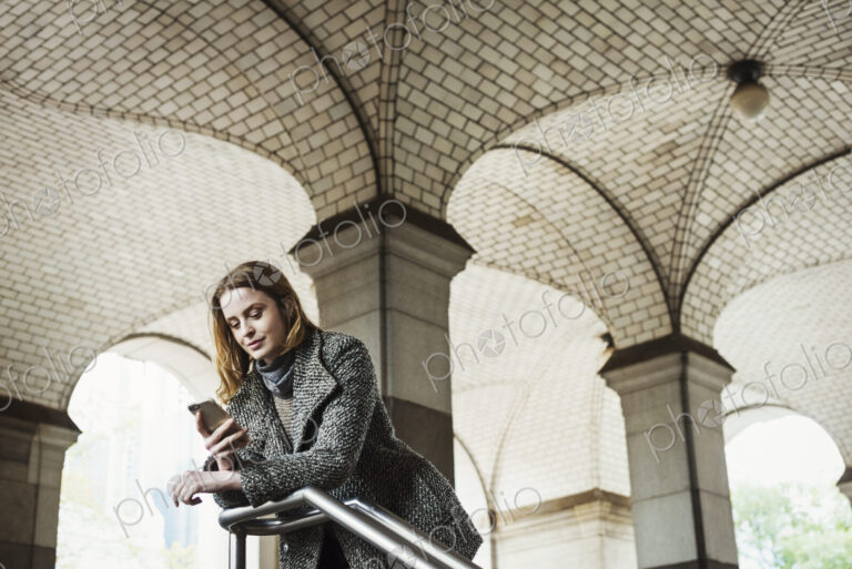 A woman with long hair looking at her smart phone, under an archway.