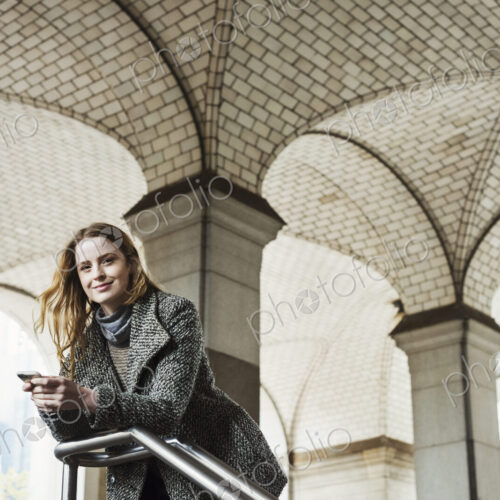 A woman with long hair looking at her smart phone, under an archway. A woman with long hair looking at her smart phone, under an archway.