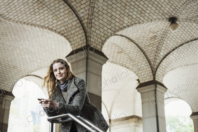 A woman with long hair looking at her smart phone, under an archway.