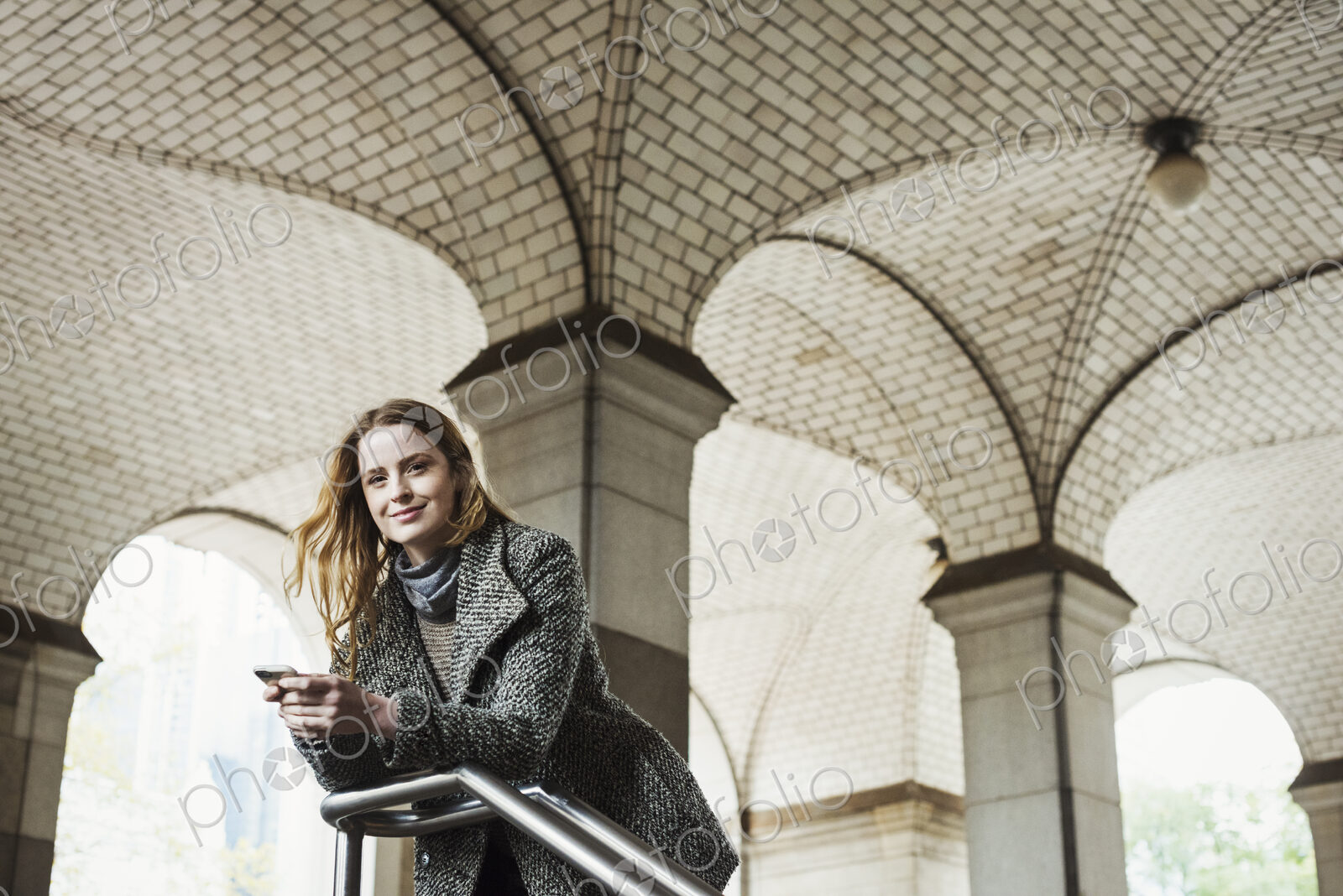 A woman with long hair looking at her smart phone, under an archway.