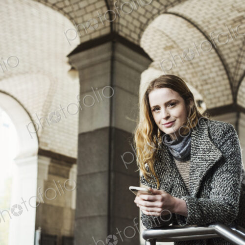 A woman with long hair looking at her smart phone, under an archway. A woman with long hair looking at her smart phone, under an archway.