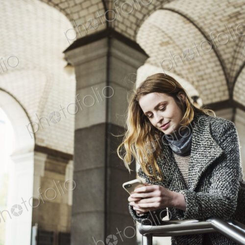 A woman with long hair looking at her smart phone, under an archway. A woman with long hair looking at her smart phone, under an archway.