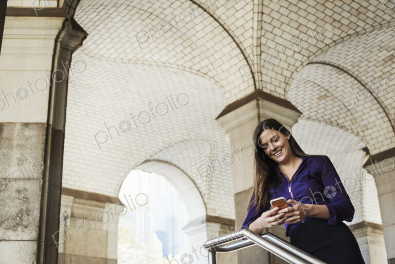 A woman with long hair standing under an arched ceiling checking her mobile phone.