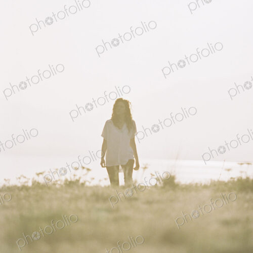 A woman with long hair wearing a white shirt standing on a grass slope.