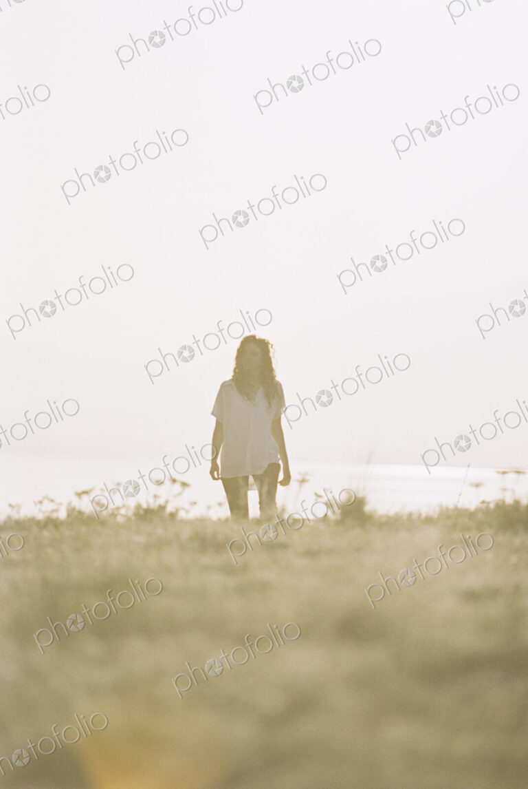 A woman with long hair wearing a white shirt standing on a grass slope.