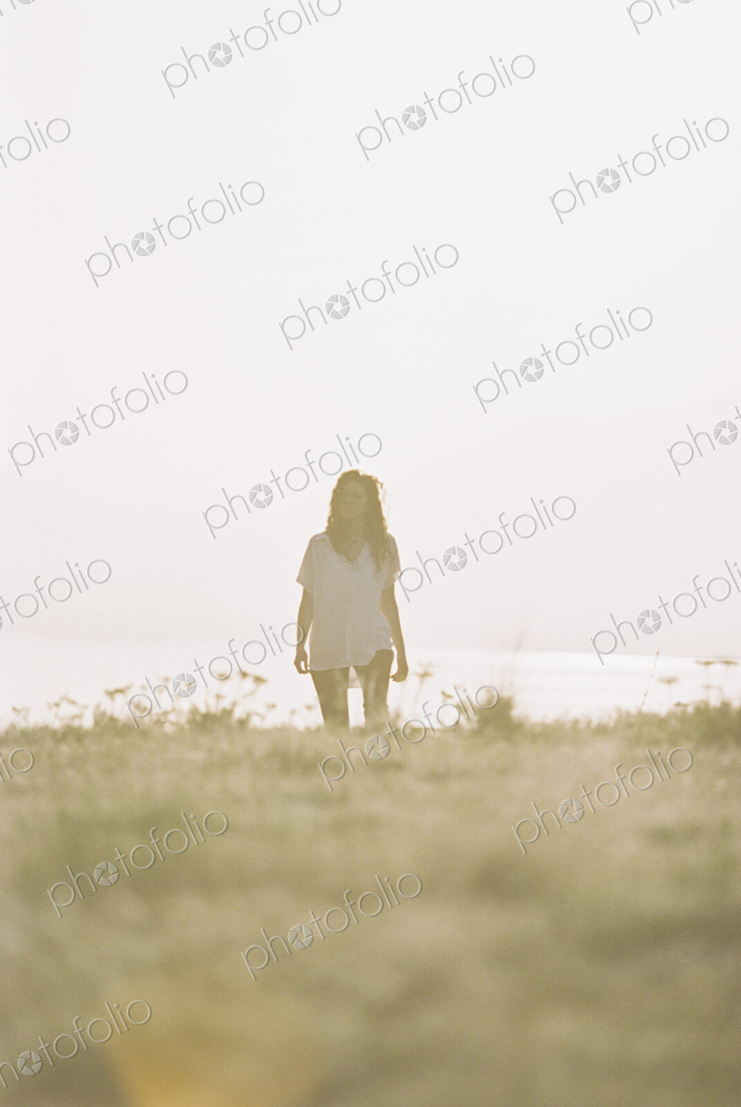 A woman with long hair wearing a white shirt standing on a grass slope.