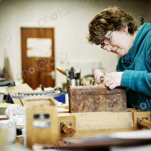 A woman working at a bench on the binding of a book in need of restoration.