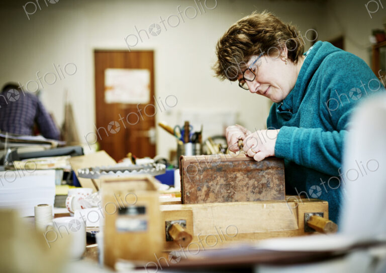 A woman working at a bench on the binding of a book in need of restoration.