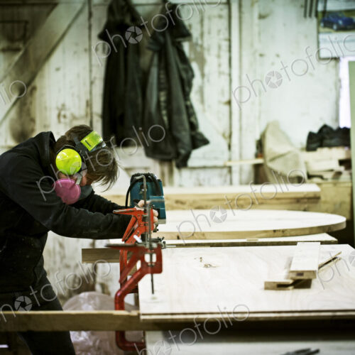 A woman working in a furniture maker's workshop cutting timber with a saw. A woman working in a furniture maker's workshop cutting timber with a saw.