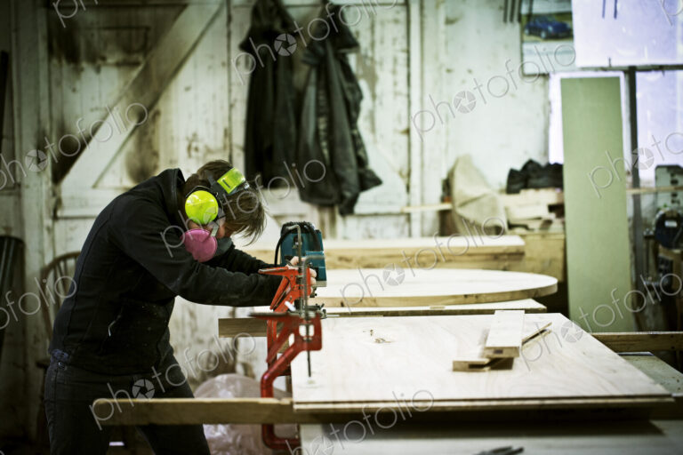 A woman working in a furniture maker's workshop cutting timber with a saw.