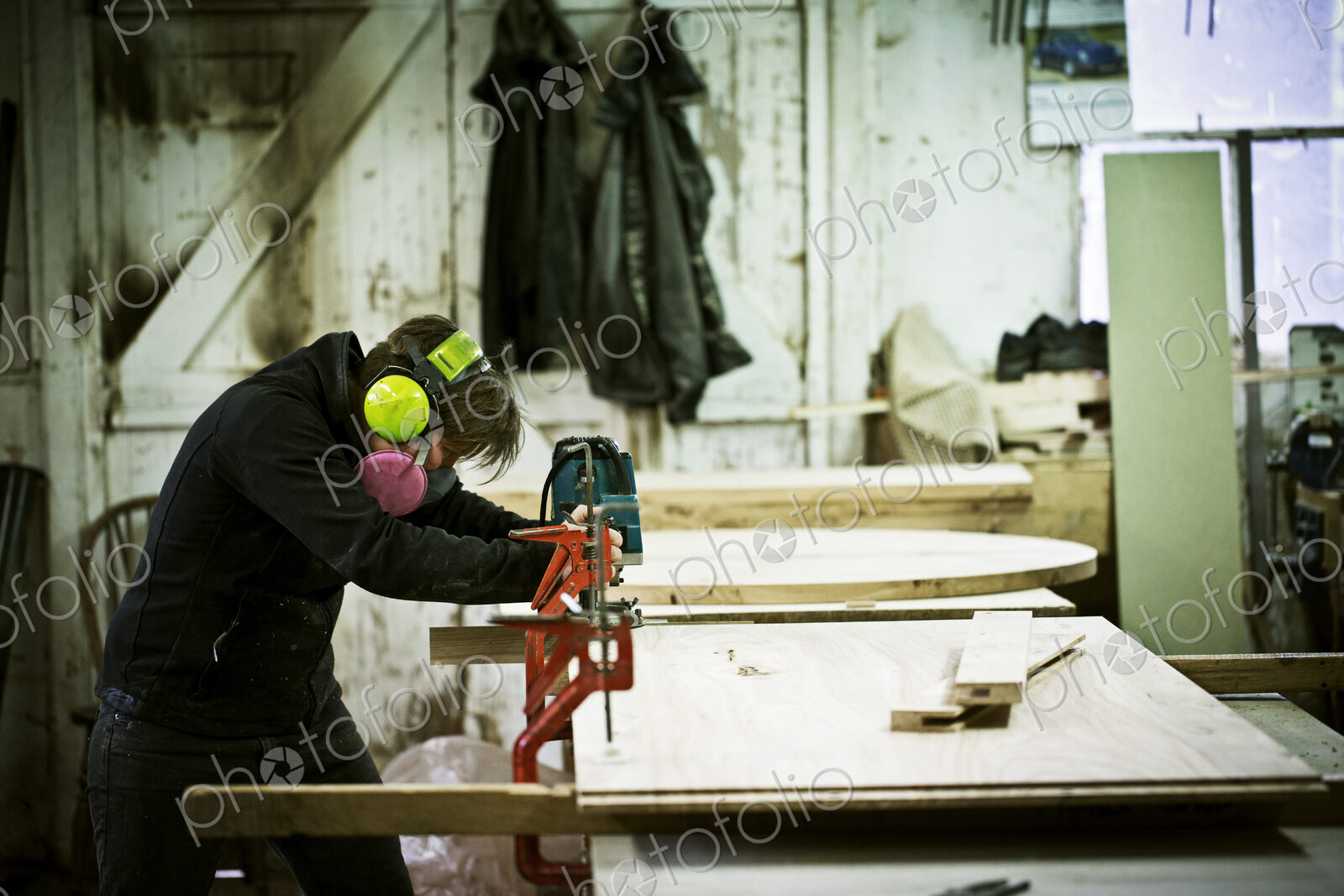 A woman working in a furniture maker’s workshop cutting timber with a saw.