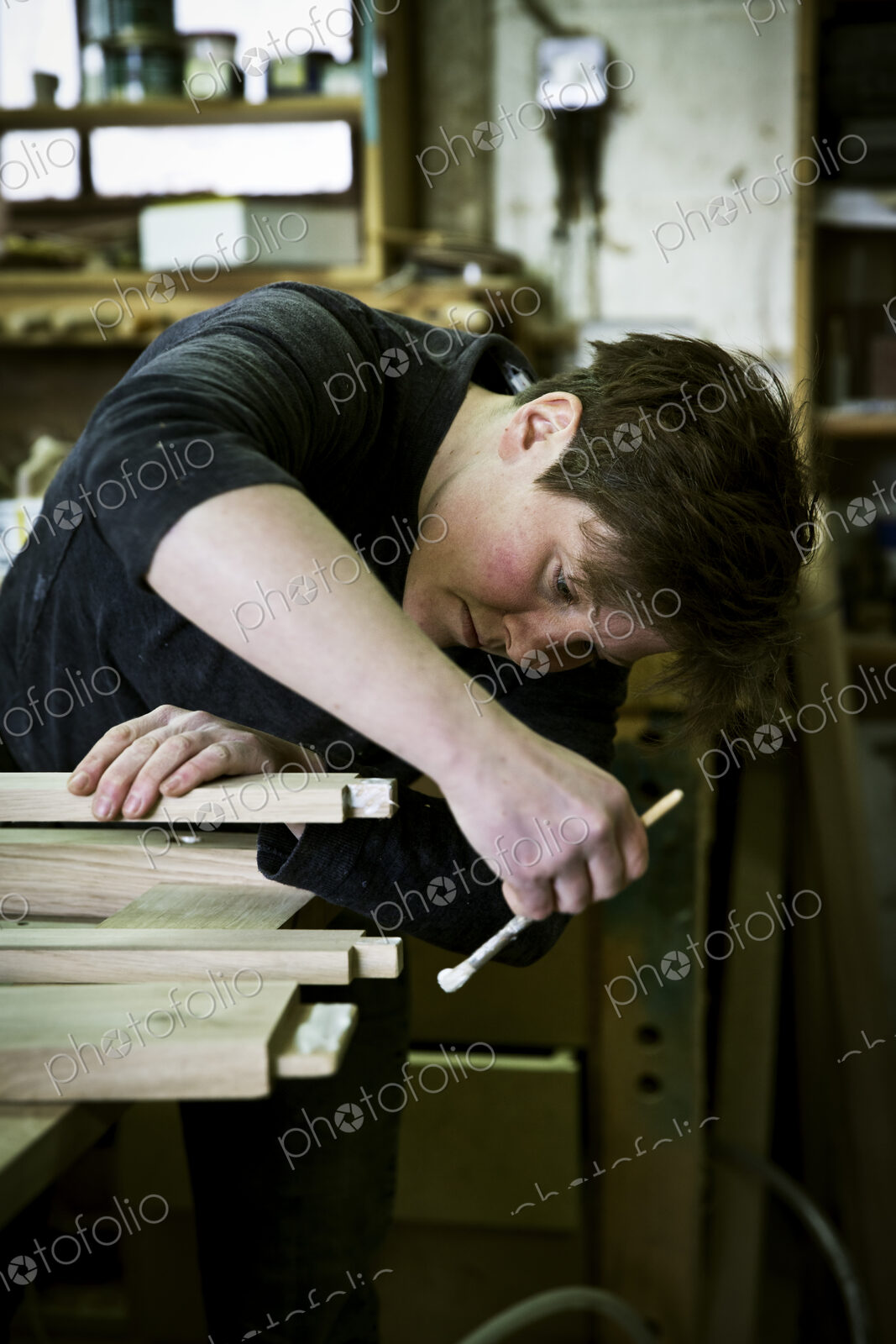 A woman working in a furniture maker’s workshop using a small brush to apply glue to…