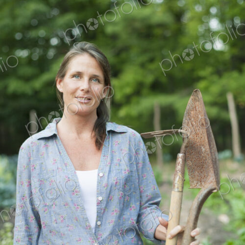 A woman working in an organic garden, standing among the vegetable crops. Holding a… A woman working in an organic garden, standing among the vegetable crops. Holding a…