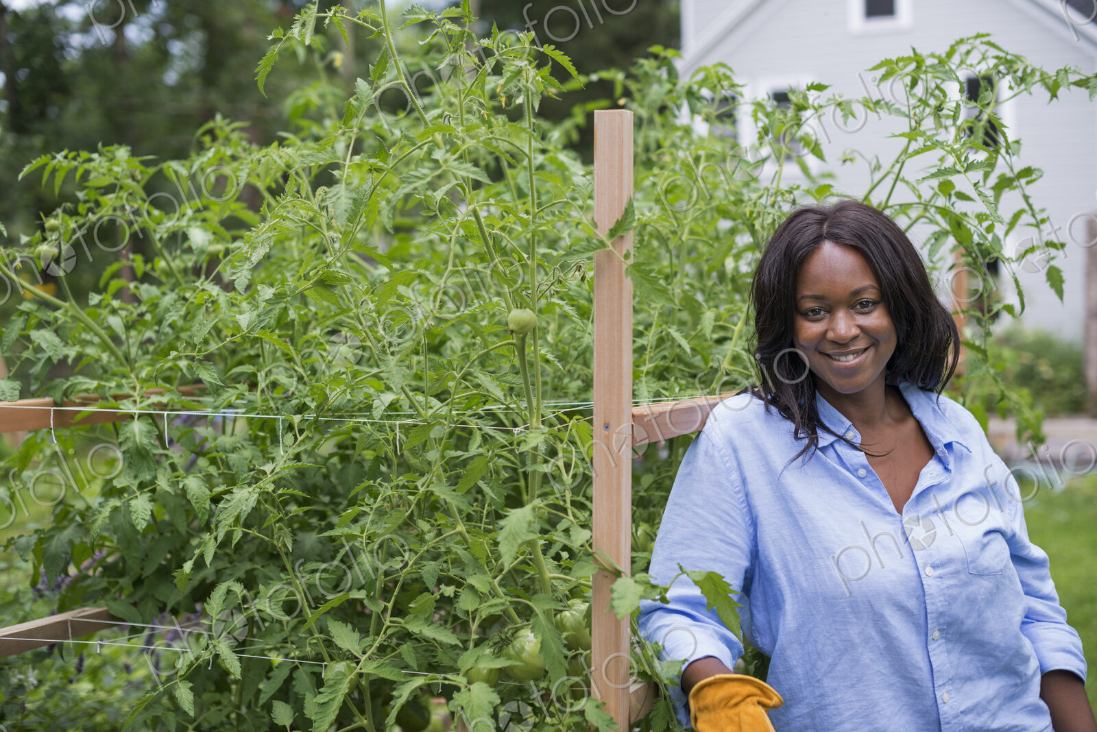 A woman working in the garden. Leaning on a fence smiling.