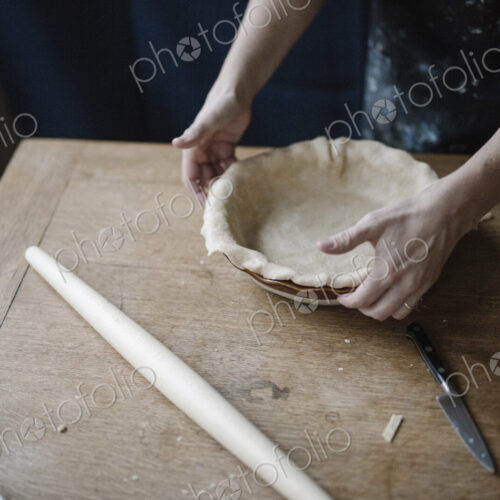 A woman working smoothing the edge of a pastry case lining a pie dish. A woman working smoothing the edge of a pastry case lining a pie dish.