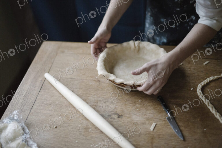A woman working smoothing the edge of a pastry case lining a pie dish.